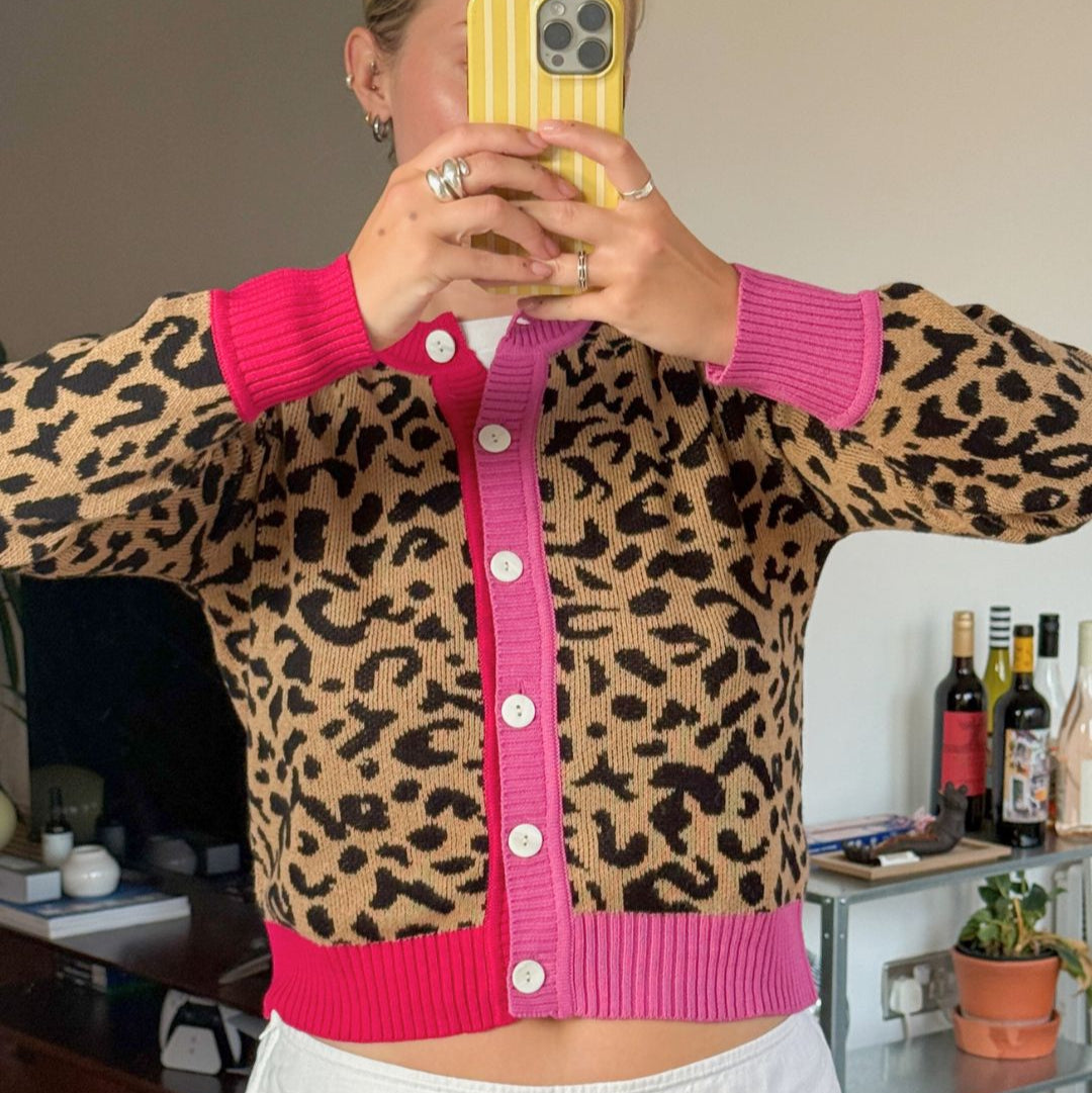 Person wearing a leopard print cardigan with pink trim, taking a mirror selfie.