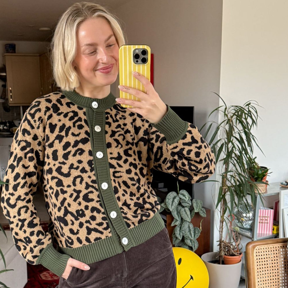 Person wearing a leopard print cardigan with green trim in a home setting.