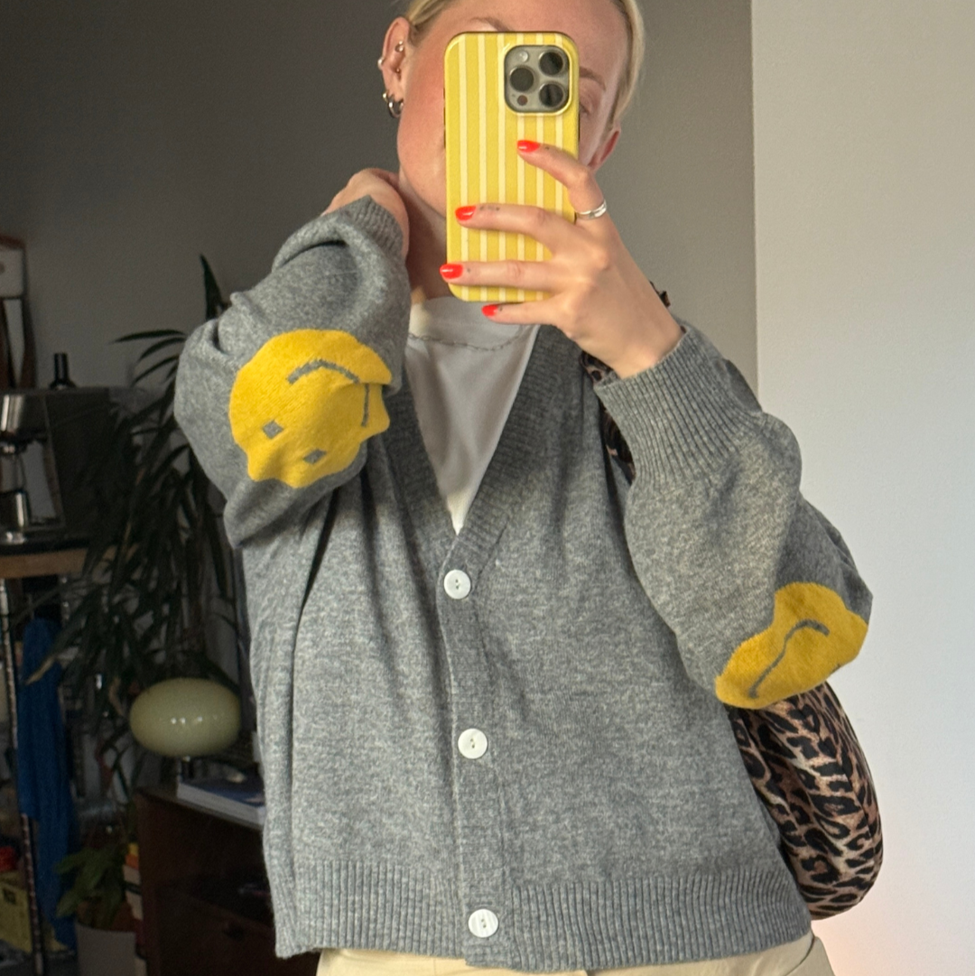 Person wearing a gray cardigan with yellow accents, holding a yellow phone case.